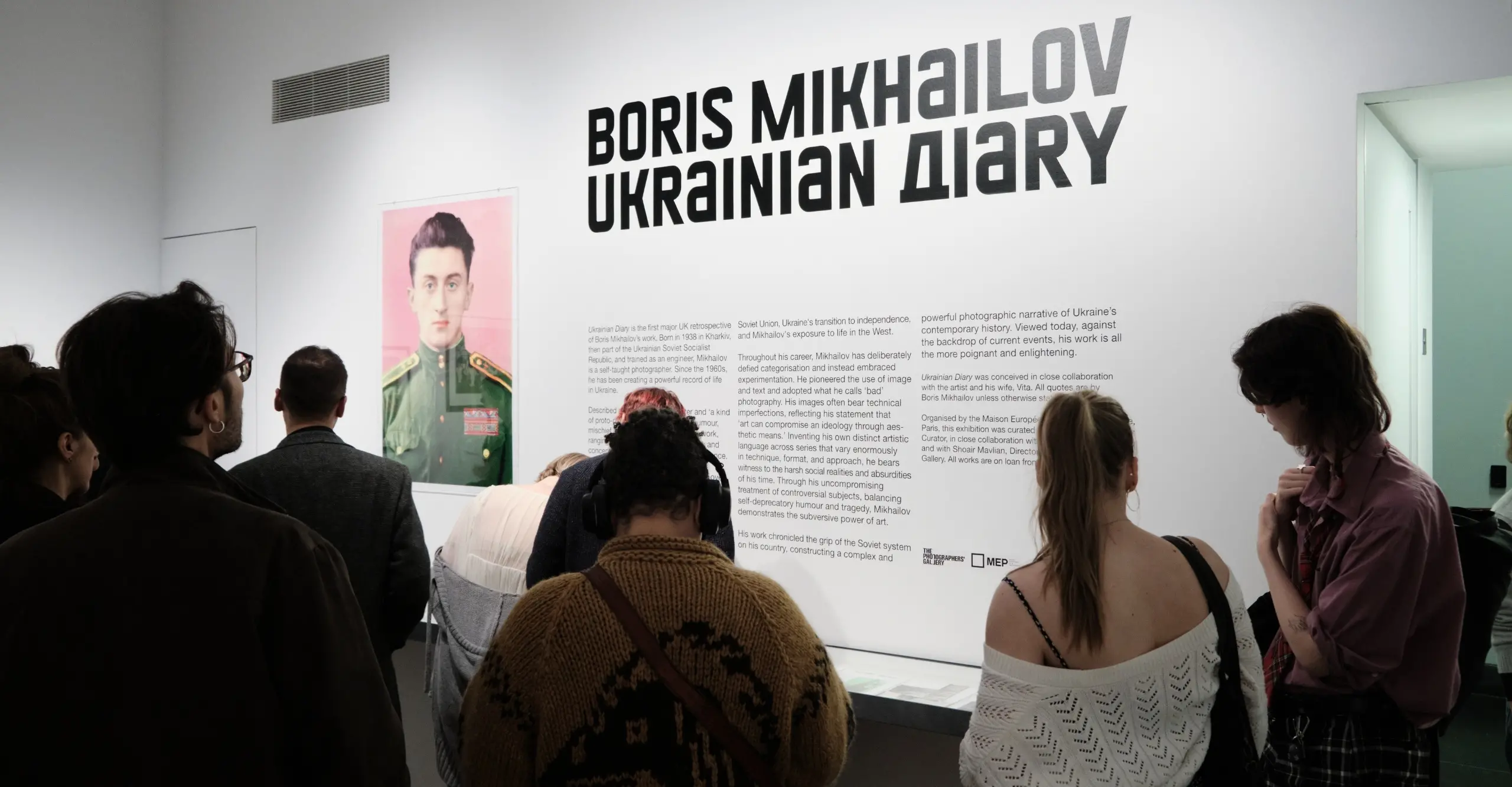 A group of people reading an exhibition wall text.