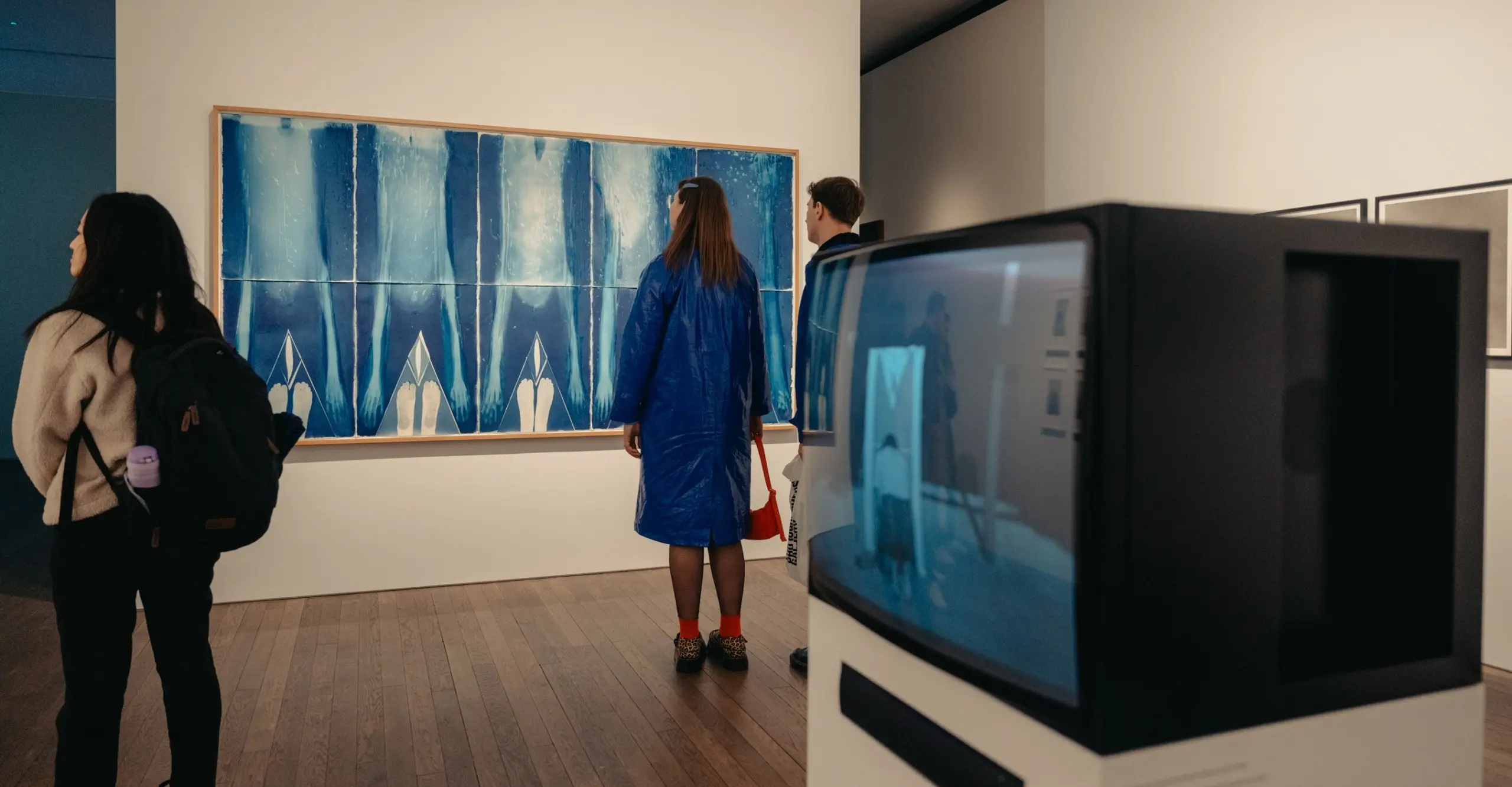 A group of people looking at large cyanotypes hung in an exhibition space.