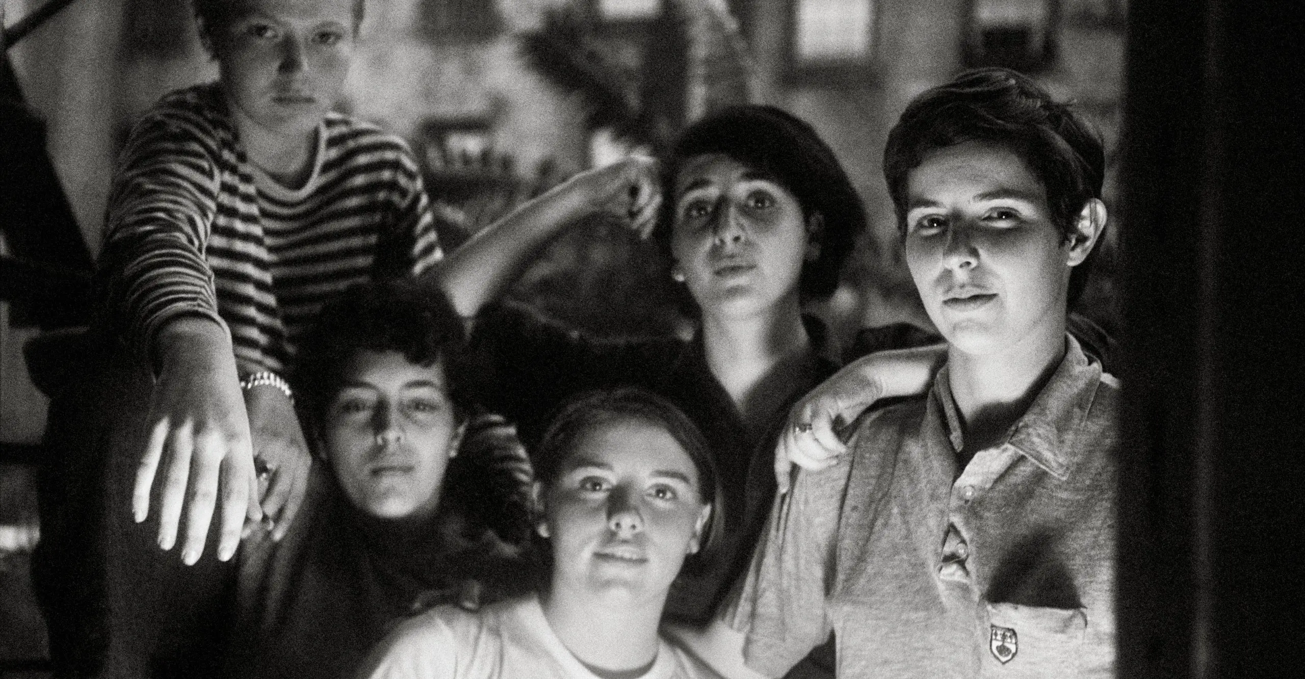 A black and white photo of a group of young queer women sat together looking toward the camera.