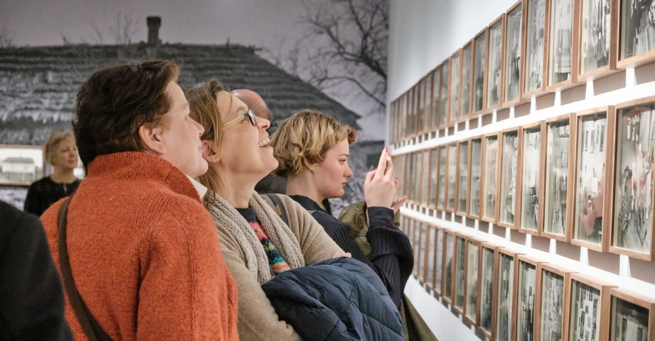 A small huddle of people looking closely at a series of framed photos hanging on a gallery wall.