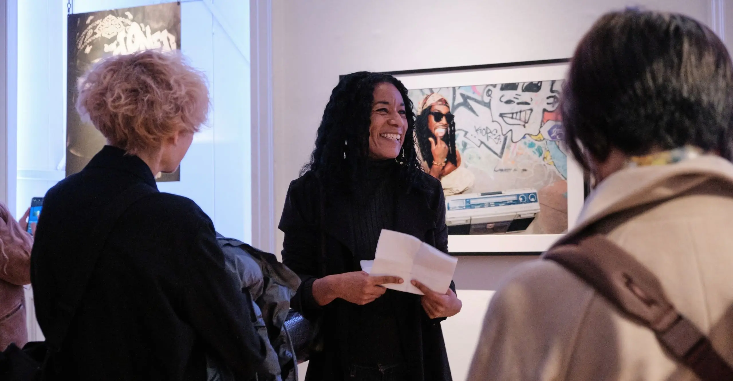 A woman stands in front of a group giving a talk. She holds a piece of paper and smiles warmly.