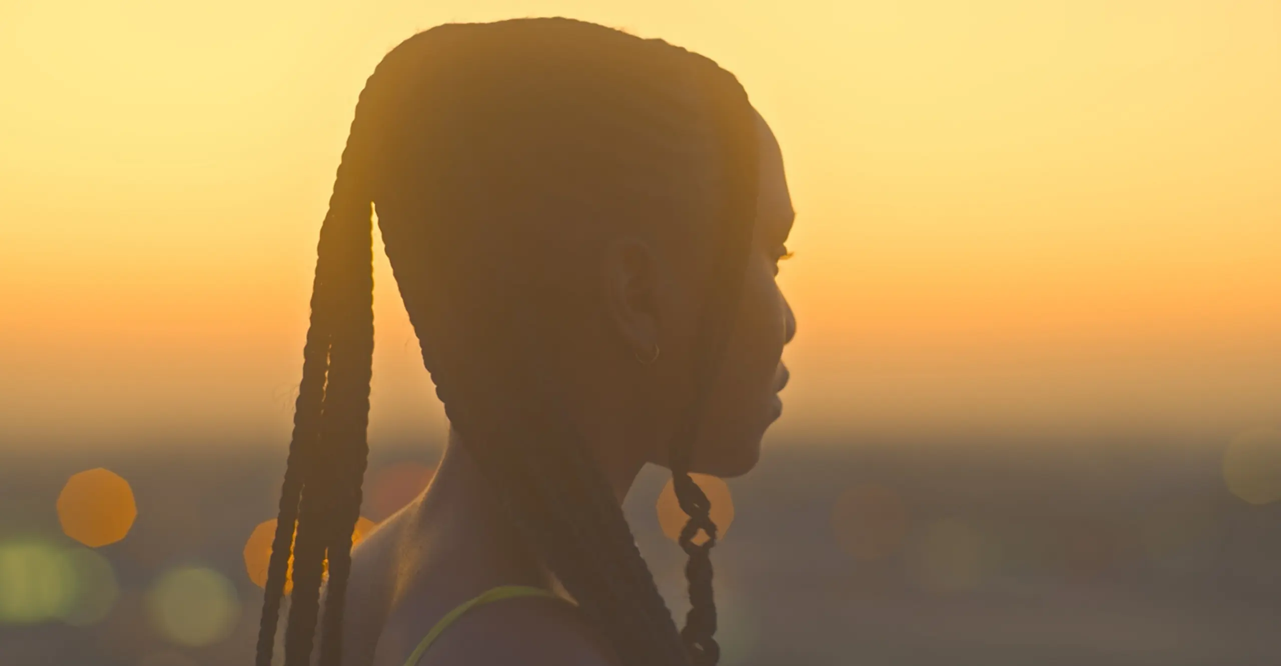 Colour film still of a woman looking off into the distance. The landscape around her shows the sun setting.