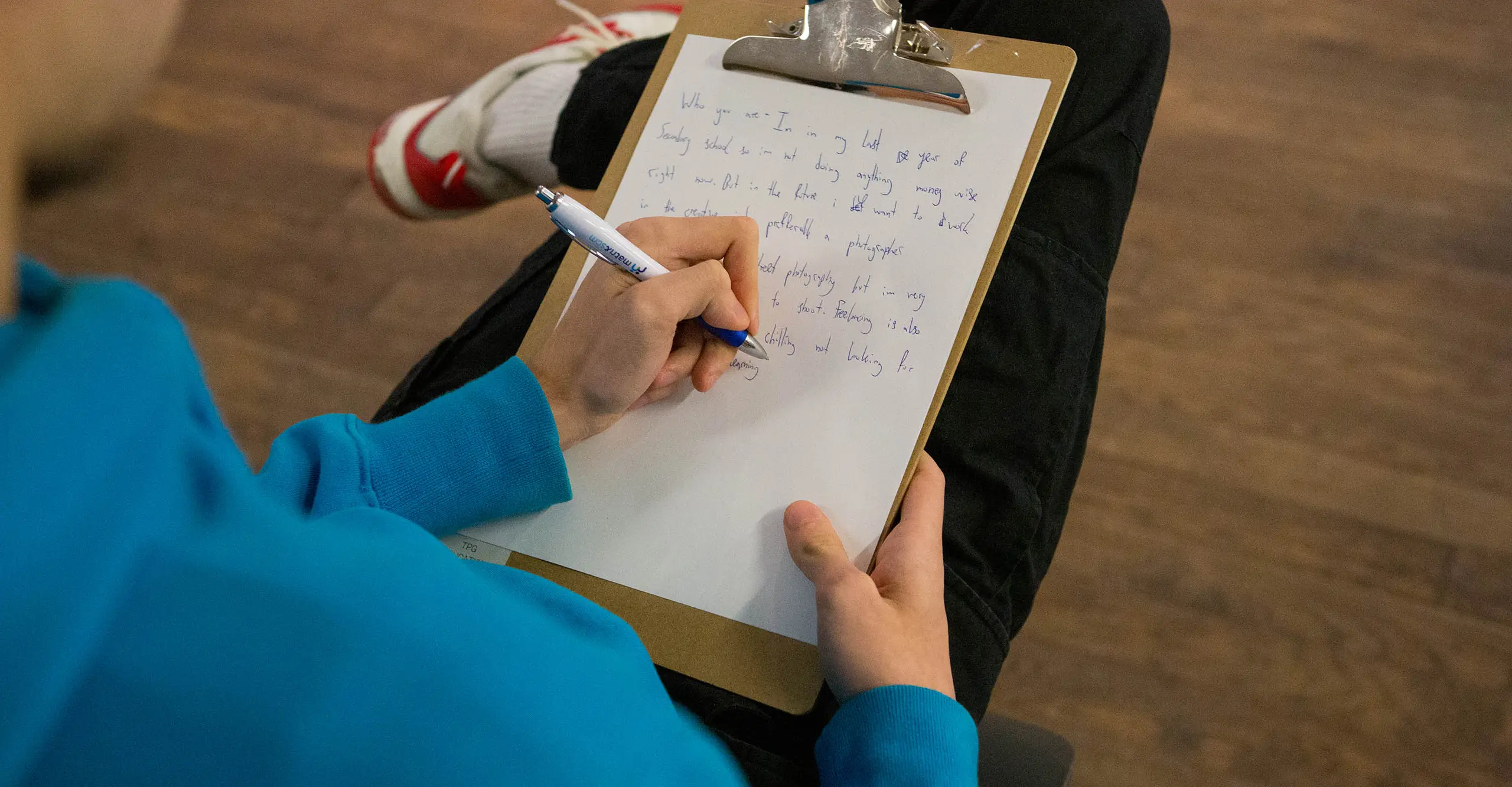 A photograph of someone sat down writing on a piece of white paper.