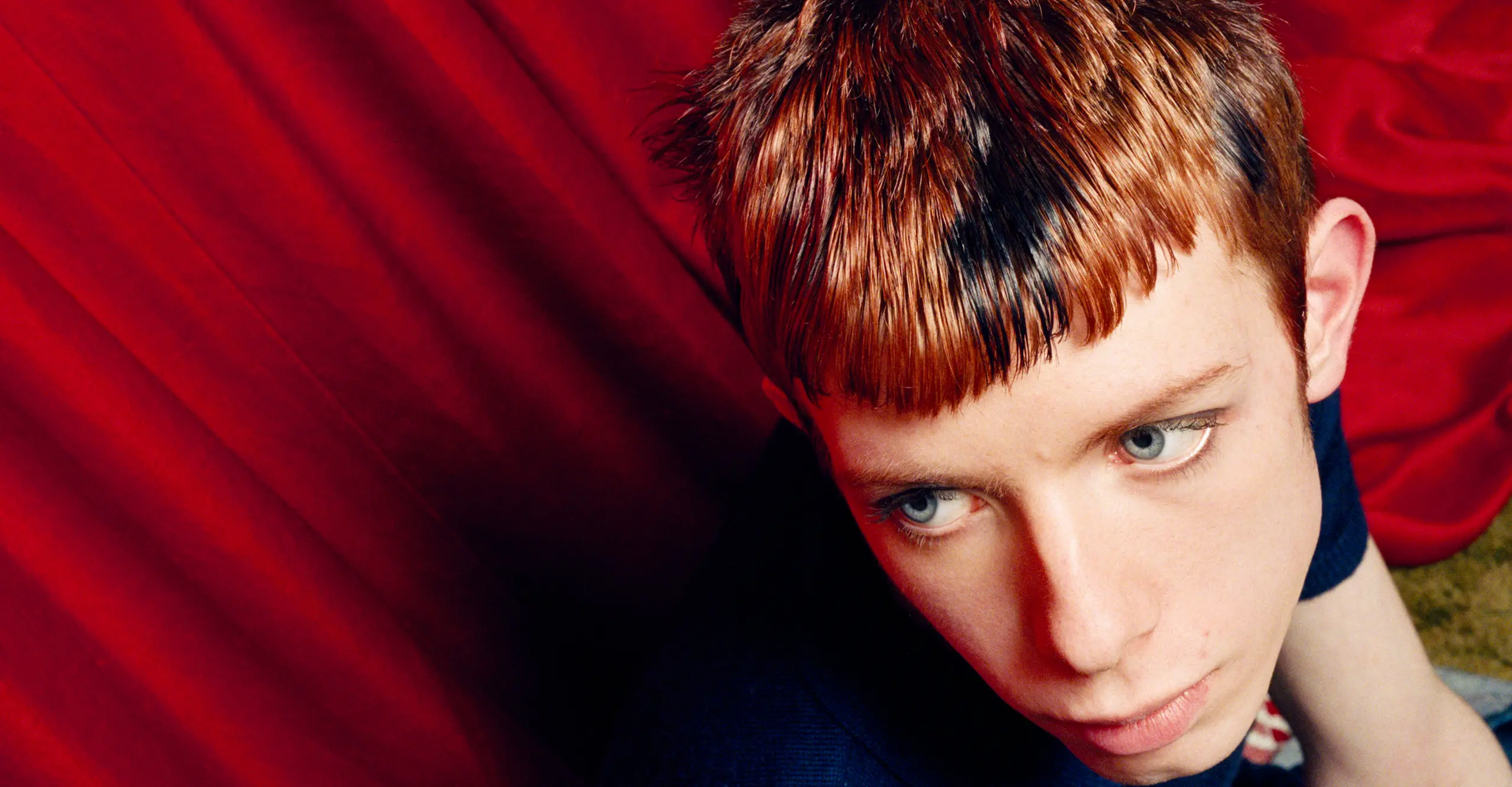 close up photograph of a boy in front of a red satin backdrop looking off to the side by marc vallee