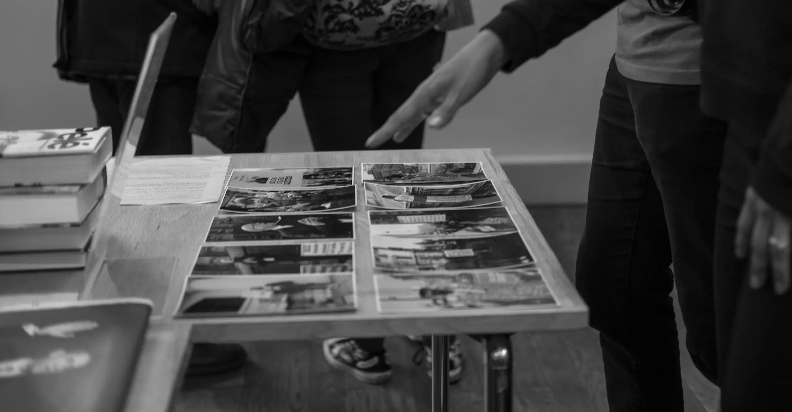 Black and white photo of a hand gesturing over a table covered in two neat rows of photographs.