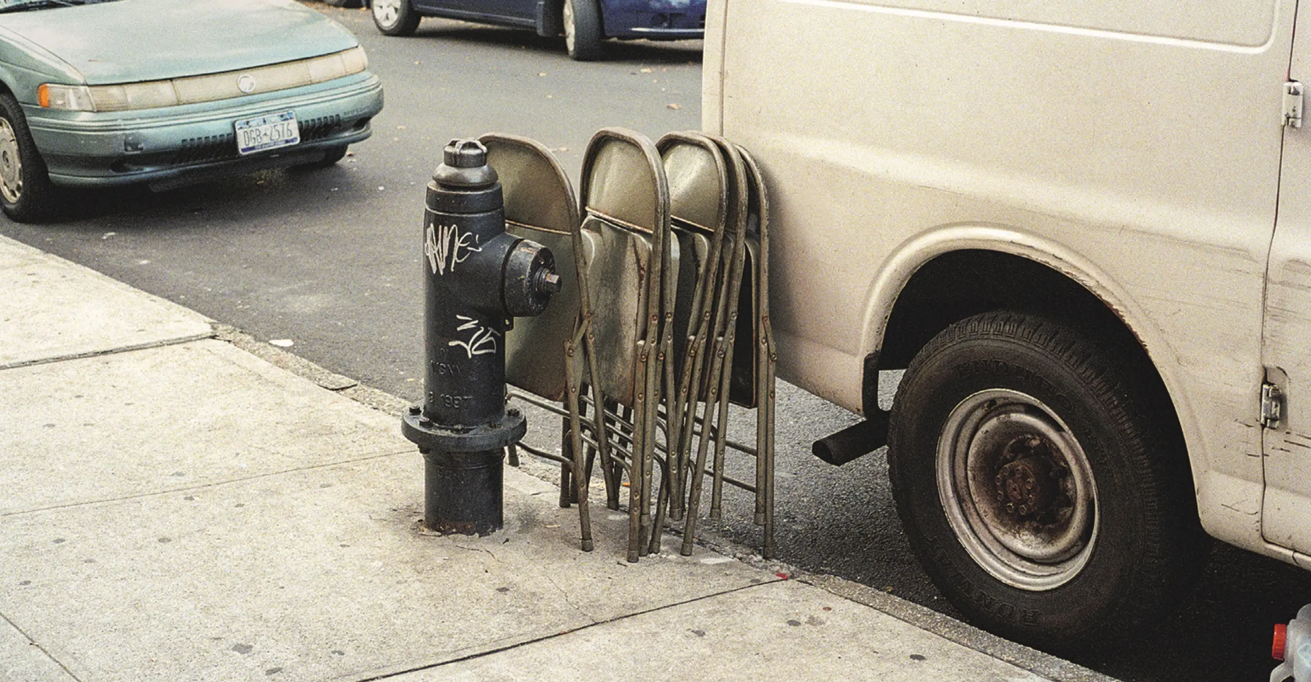 Street scene showing  a black fire hydrant and green chairs leaning a against a parked white van