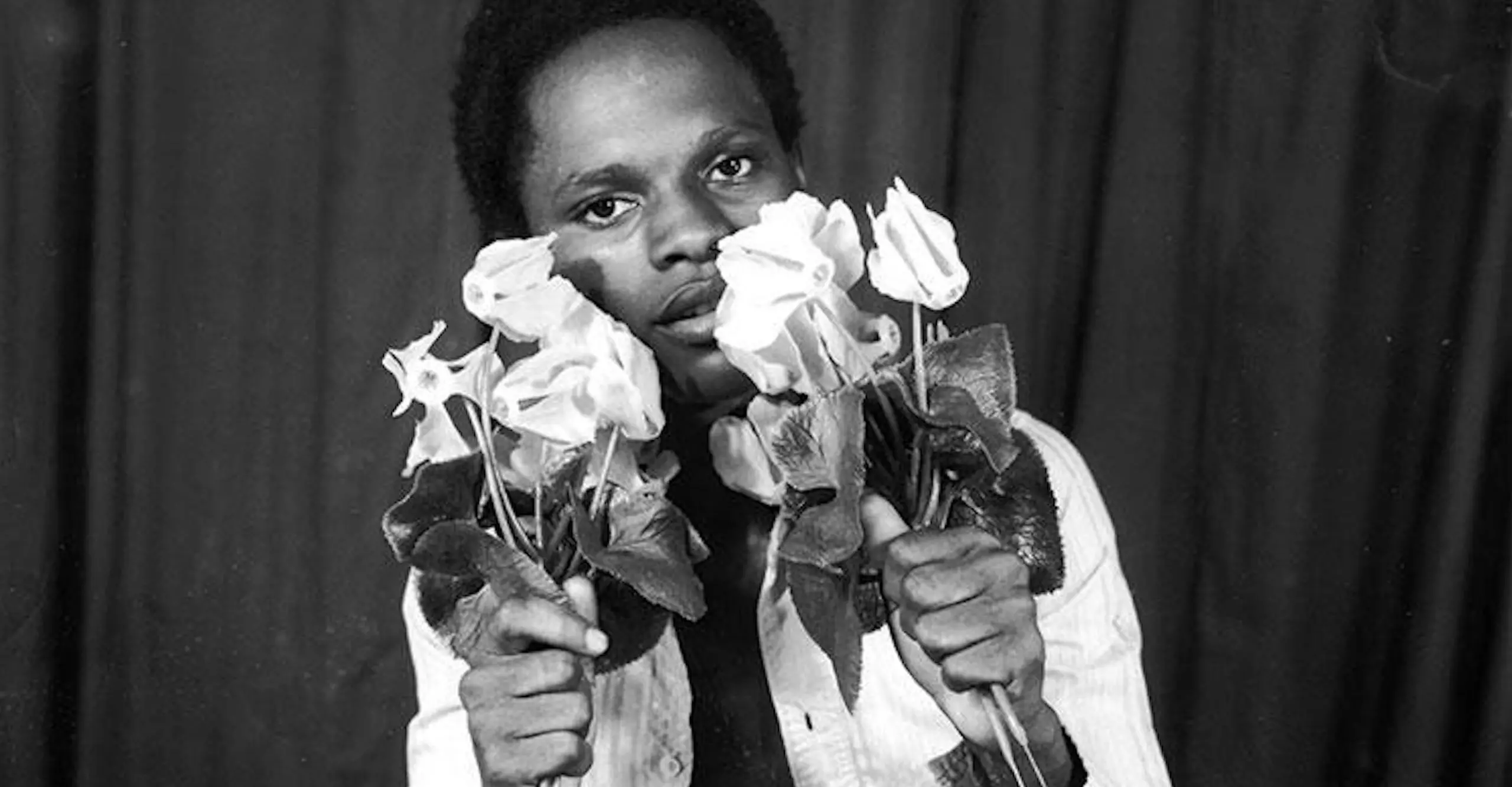 A young man holds flowers to his face in a studio portrait