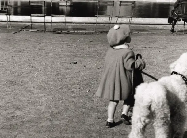 Black and white photograph of a young person holding a dog on a lead in a Paris park