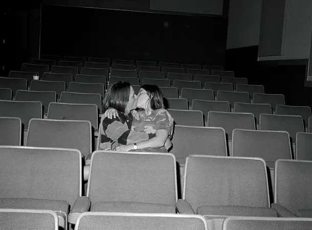 Black and white photograph of two people holding each other and kissing in a cinema