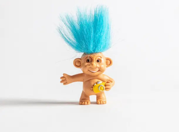 A plastic troll toy with a big smile and bright blue hair sticking upwards.