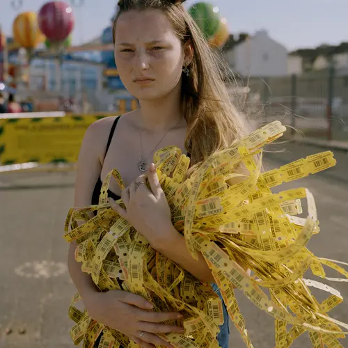 An image of a young girl on a beach holding a large amount of yellow arcade tokens in long strips spilling out of her arms.