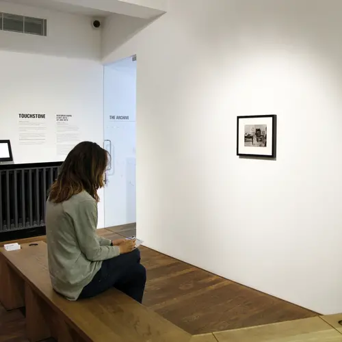 Person seated on a bench in front of a framed black and white photograph.