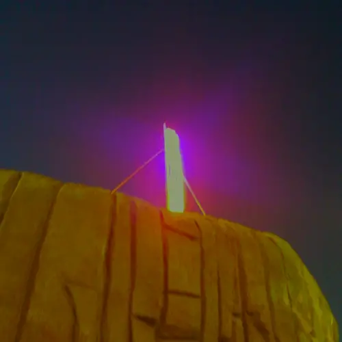 A colour photograph of a shiny pink pole on top of a cliff in the night.