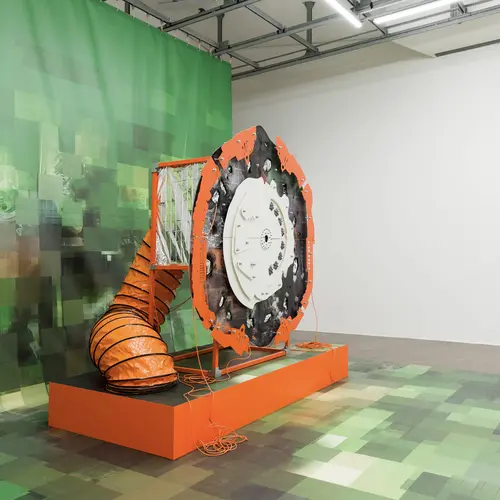 Install image from V2: Rigged where a sculpture built to look like a previously generated image captures itself through an installed camera reflected back itself in a mirror.