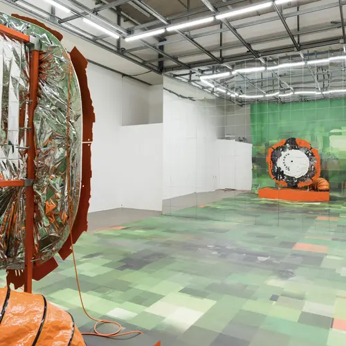 Install image from V2: Rigged where a sculpture built to look like a previously generated image captures itself through an installed camera reflected back itself in a mirror.