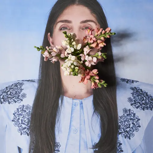 A photograph of a person against a blue background with a bunch of flowers coming out of their mouth. 