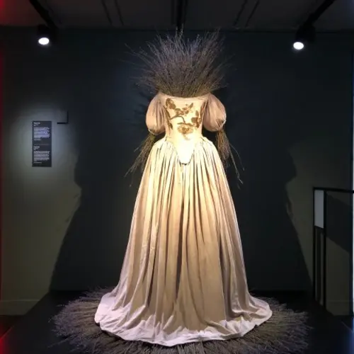 A white dress in a gallery, with lavender coming out of the holes where a head and two arms would be