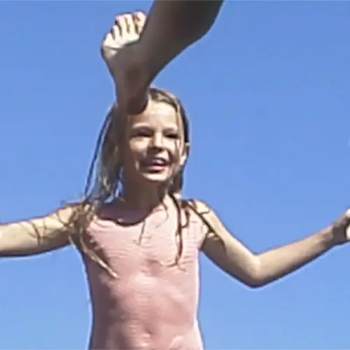 A photograph of a girl smiling and jumping in front of a blue sky 
