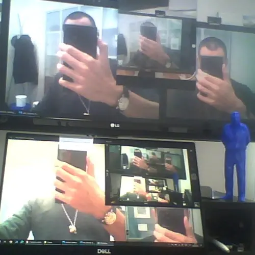 A photograph of several screens showing the same person holding a phone in front of their face