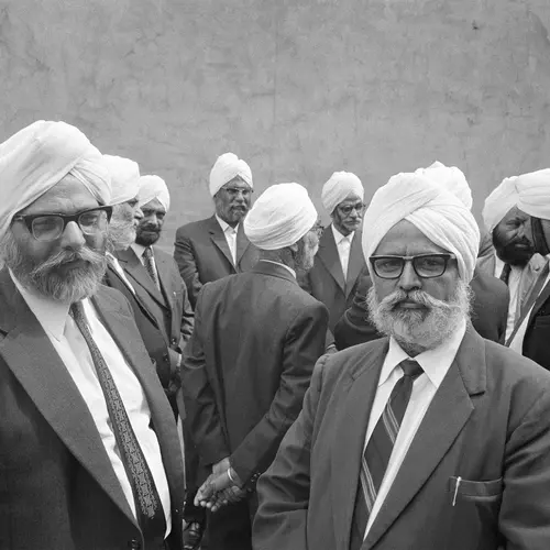 Black and white photograph of several older man dressed in suits and turbans standing and talking with each other.