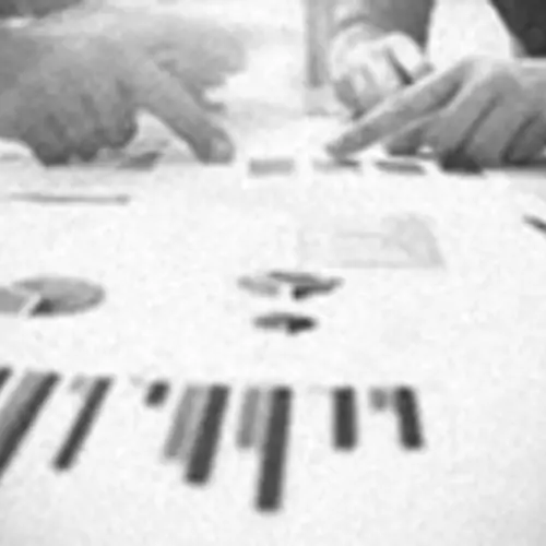A black and white close up photograph of the hands of two people pointing to printed graphs on a table