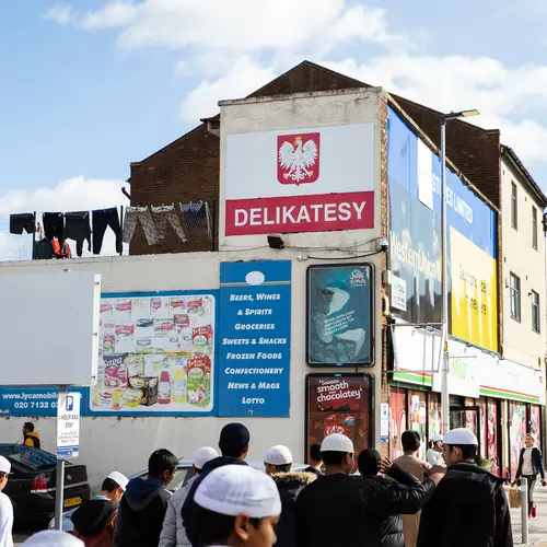 A group of young schoolboys wearing white prayer hats cross the street by a Polish delicatessen. 