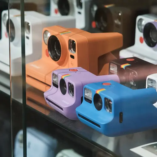 Colourful Polaroid cameras inside a glass display case.