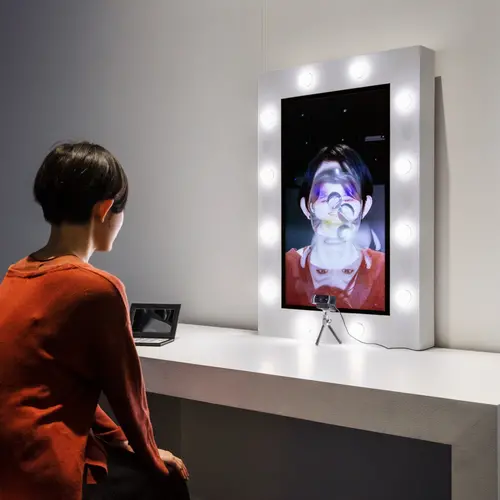 A young woman looks into a screen, which shows an augmentation of her face