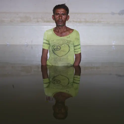 Photograph of a man half submerged amidst floodwaters in his Pakistan home wearing a pale green peace & love worn t-shirt