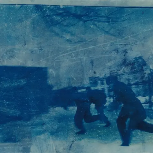  Blue toned photograph of three men  running in the direction of a building.