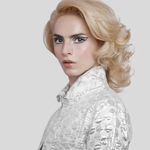 Photograph of a person with blonde hair, wearing a silver blazer