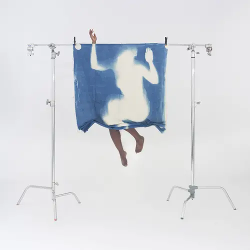 a suspended blue print of a womans body, a woman jumops behind it, matching her legs and arms to the image