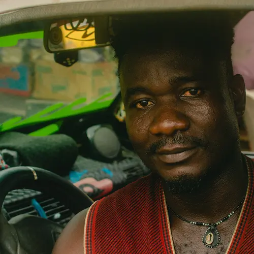 A portrait of a cab driver called Mr. Ifeanyi, who looks directly into the lens. Behind him, to the left, you can see his dashboard, which displays important items to help him navigate his day. ⁠