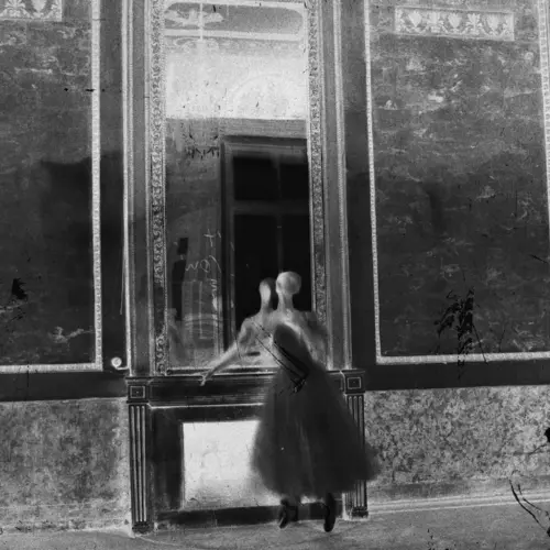 Inverted black and white photograph of a female figure standing in a room.