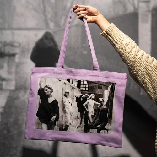 Colour photograph of a person's hand holding up a Debroah Turbeville themed tote bag.