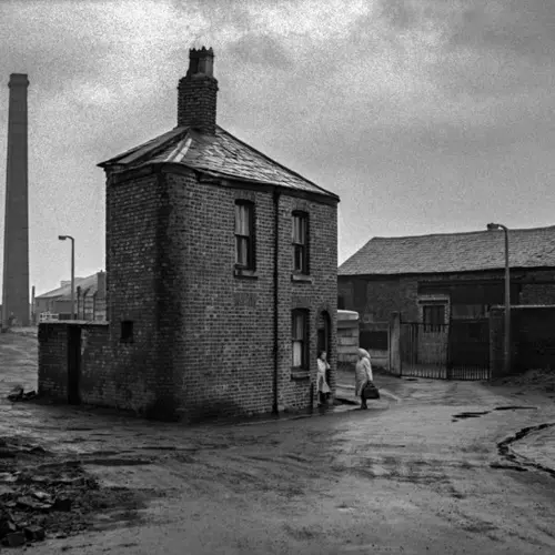 Black and white photograph of a stand alone house in urban, industrial landscape