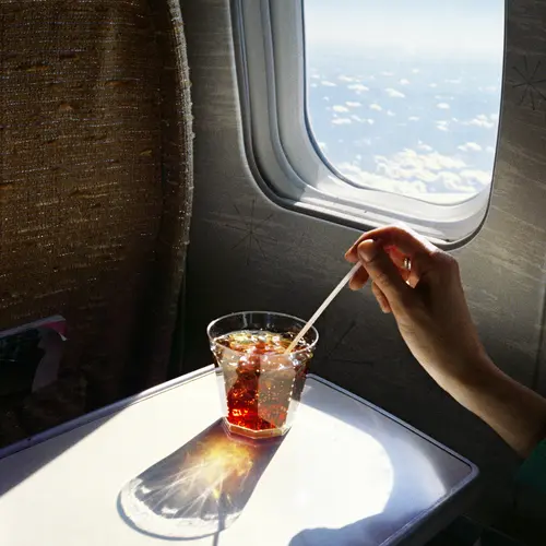 Colour photograph of a drink placed on a folded-down tray-table within the cabin of a plane.