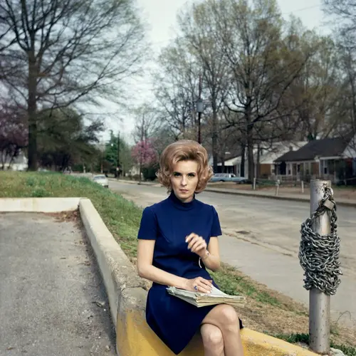 Colour photograph of a woman sitting on the edge of the yellow kerb.