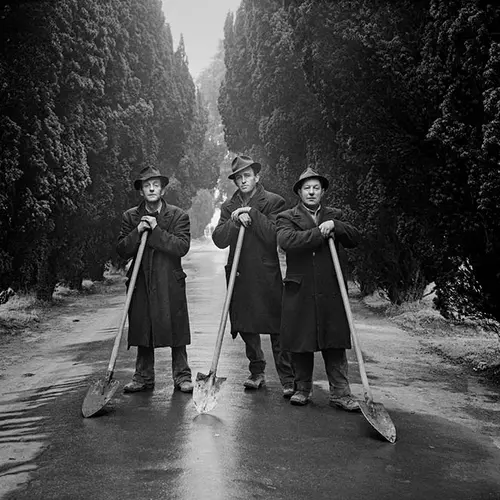 Black and white image of three men stood leaning on long shovels