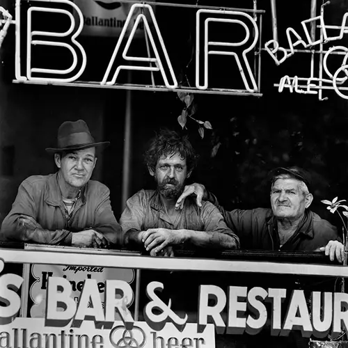 Black and white photograph of three men sat in the window of a bar