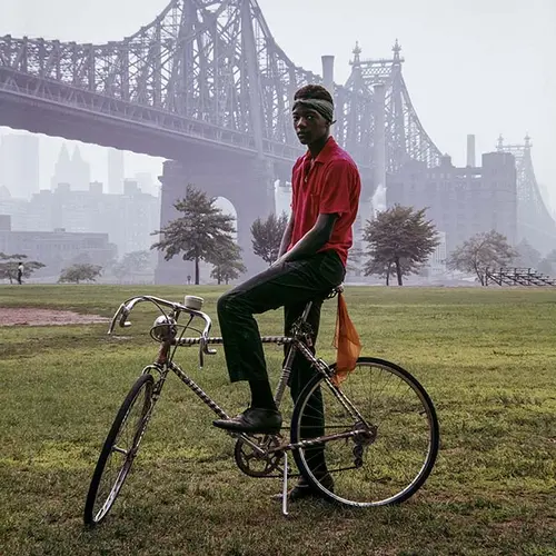 young man sat on bicycle with bridge in background and grass in foreground