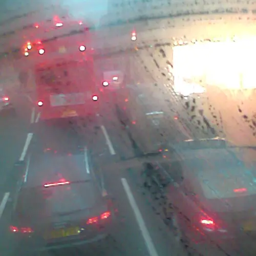 A photograph of a road with a red bus and some cars, taken from above through glass with condensation