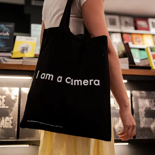 A close shot of a person wearing a black tote bag which features a white line of text. The text says "I am camera".