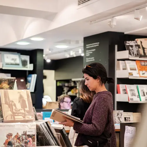 A woman is pictured flipping through a book with a focused expression on her face. 