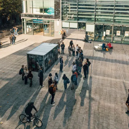 Install image from V1: Content Aware in which a large shipping crate installed with a camera is capturing images of itself in a mirrored window.