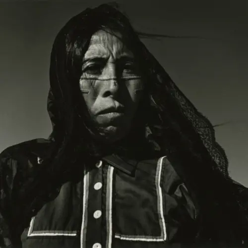 Black and white portrait photograph of a woman with indigenous paintings on her face and a black veil over her head.
