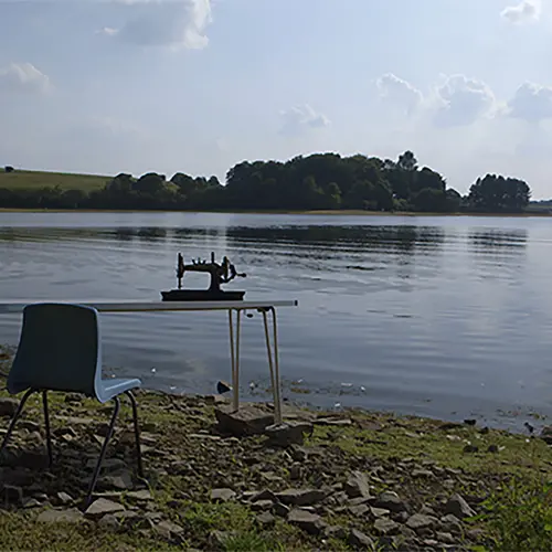 A sewing machine is positioned on a table in front of a lake