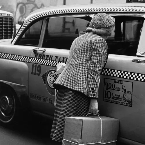 A lady with a large cardboard box hails a New York taxi