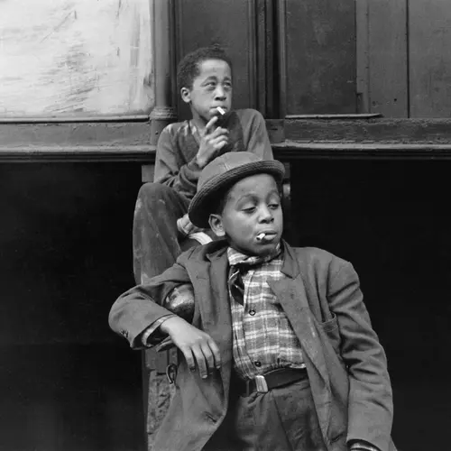 Two young boys slouch in a doorway. They are both smoking.