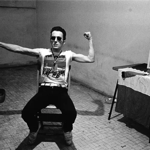 black and white photograph of joe strummer sitting on a chair posing